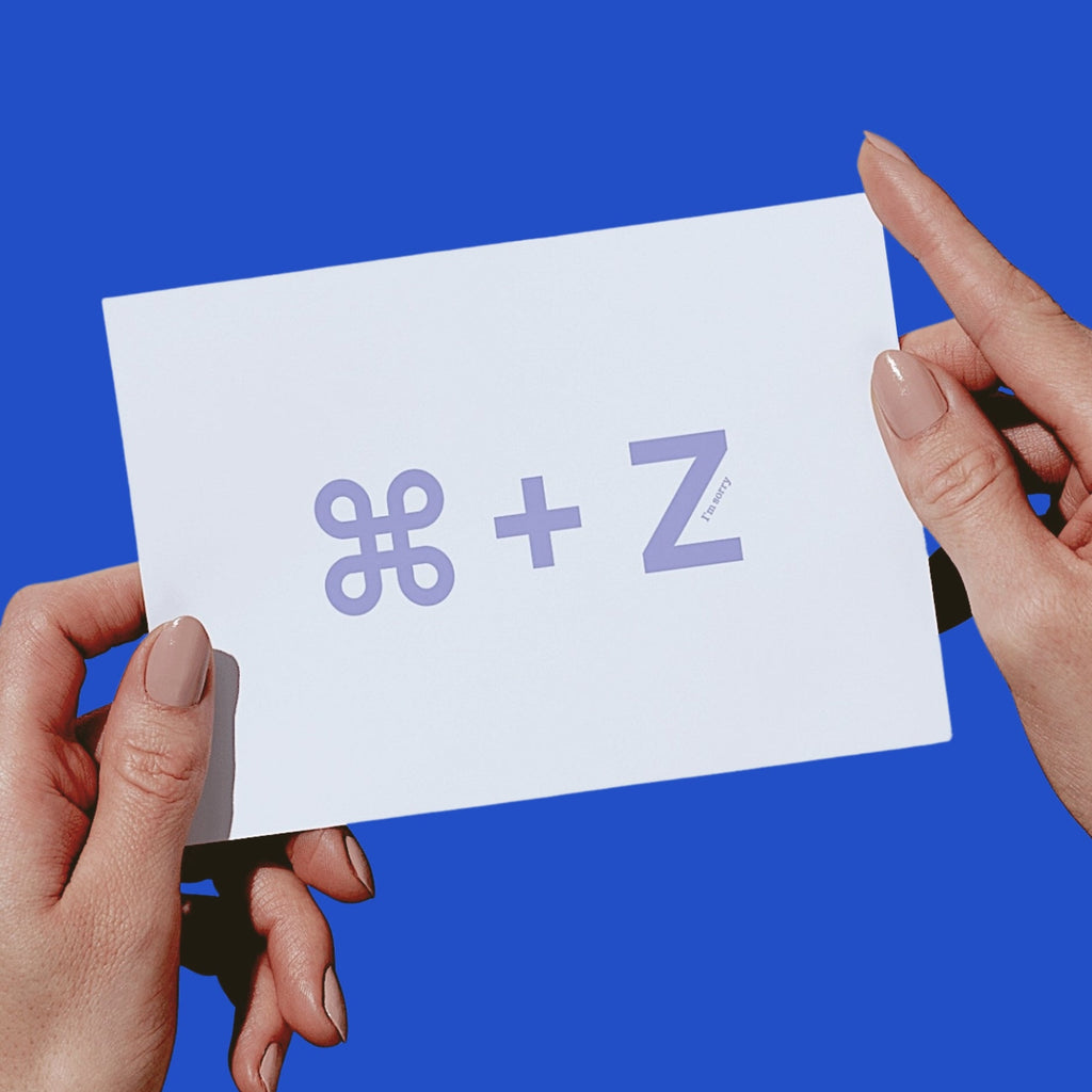 Two hands holding a white card with a lavender-colored 'COMMAND - Z' symbol against a solid blue background.