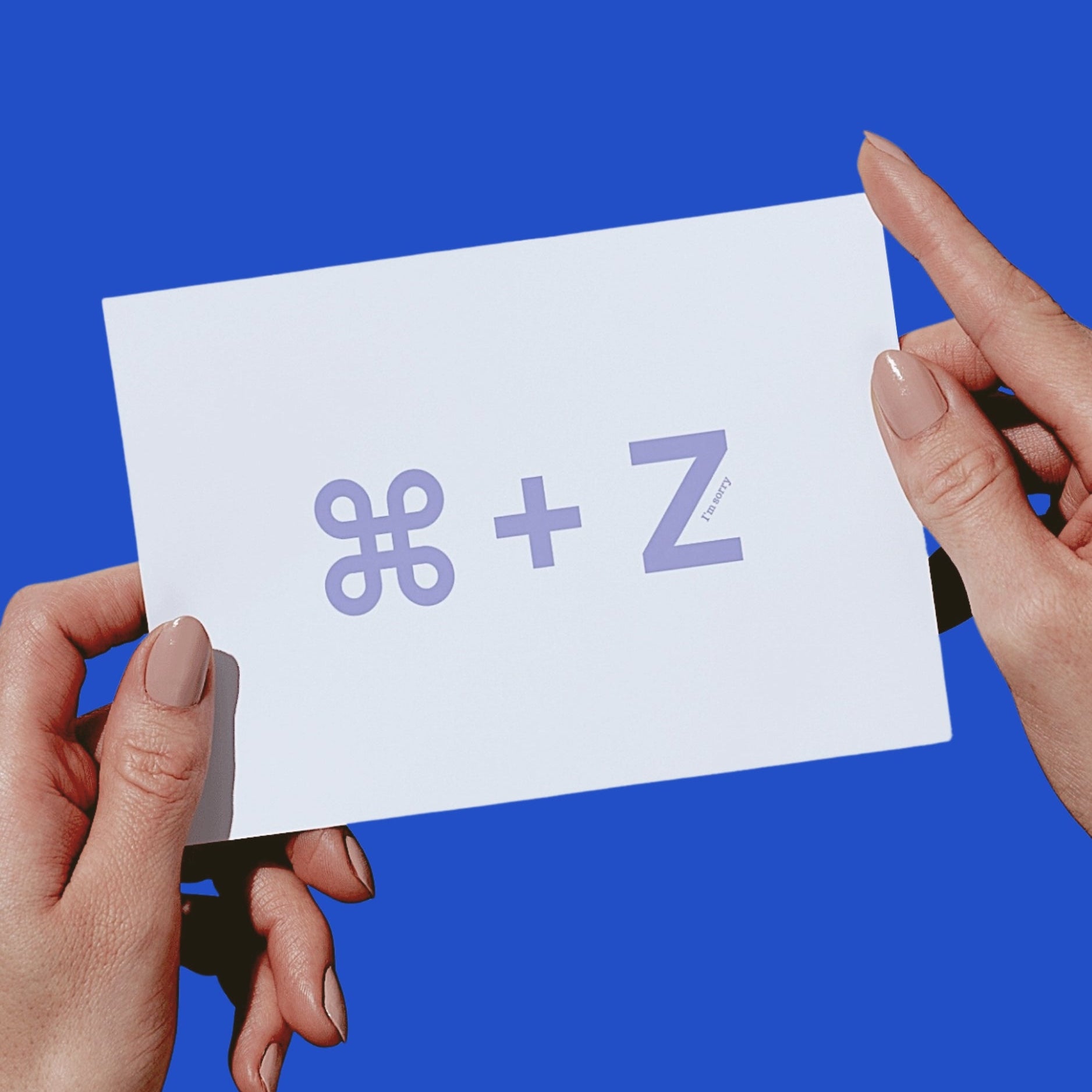 Two hands holding a white card with a lavender-colored 'COMMAND - Z' symbol against a solid blue background.